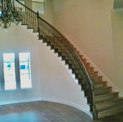 Sweeping curved staircase with wood treads and decorative dark iron balusters